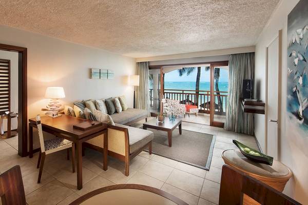 Innenansicht einer Suite im Constance Belle Mare Plage Hotel mit Wohnzimmer, Essbereich und Blick auf den Ozean.