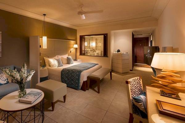 Suite-Zimmer im Constance Belle Mare Plage Hotel mit Doppelbett, Sofa, Tisch und Dekor.