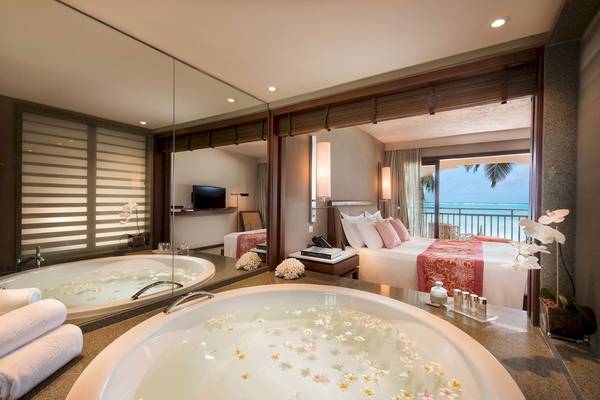 Innenansicht einer Suite im Constance Belle Mare Plage Hotel mit Badewanne und Bett.