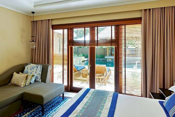 Schlafzimmer des Constance Belle Mare Plage Hotels mit Bett, Couch, Sessel und Swimmingpool im Hintergrund.