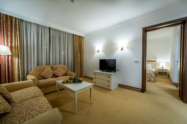 Wohnbereich im Helena Sands Hotel mit Sofas, Tisch, Fernseher und Schlafzimmerzugang.