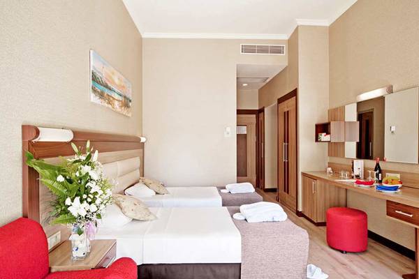 Suite-Zimmer im Sueno Hotels Beach Side mit zwei Betten, Tisch, rotem Stuhl und Blumen.