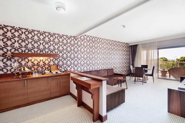 Innenbereich einer Suite im Sueno Hotels Beach Side mit gemusterten Wänden, Couch, Esstisch und Balkon.