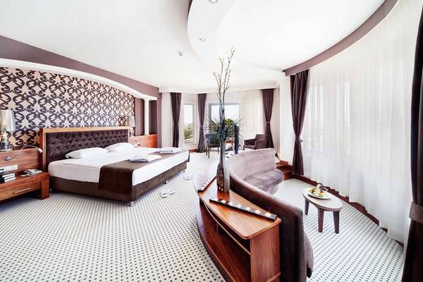 Innenansicht eines Hotelzimmers im Sueno Hotels Beach Side mit Doppelbett, Wohnzimmerbereich und Blick auf die Stadt.