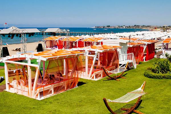 Foto von Sueno Hotels Beach Side Terrasse mit orangen Vorhängen und Sonnenliegen auf dem Rasen.