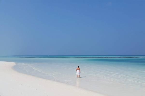Eine Person in einem weißen Handtuch steht auf dem weißen Sandstrand des Meeru Island Resorts & Spa.