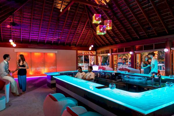 Bar-Lounge im Meeru Island Resort & Spa mit blauer Beleuchtung und freundlichen Gästen.