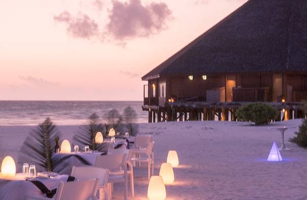 Romantisches Abendessen am Strand im Meeru Island Resort & Spa mit Blick auf das Meer und eine Hütte.