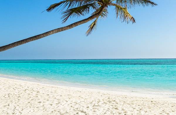 Ein Paar am Meeru Island Resort & Spa Strand, neben einer ankernden kleinen Boot.
