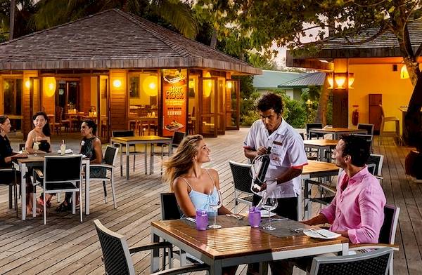 Außenbereich des Meeru Island Resorts & Spa mit Gästen an Tischen und einem Kellner.