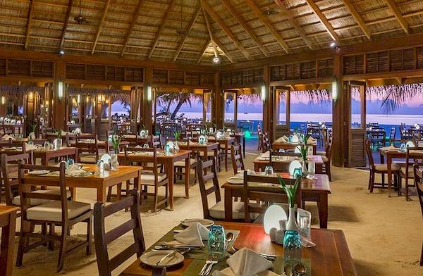 Innenbereich des Meeru Island Resort & Spa Restaurant mit vielen gedeckten Tischen und Blick auf das Meer.