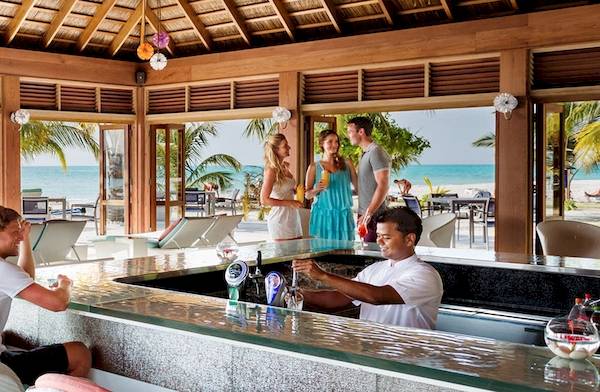 Barbereich im Meeru Island Resort & Spa mit Blick auf das Meer und Gäste, die Cocktails genießen.
