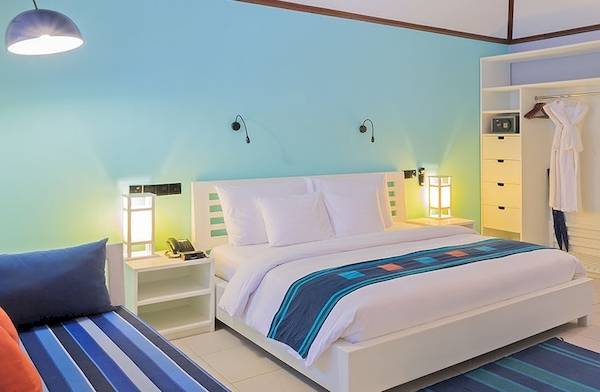 Schlafzimmer im Meeru Island Resort & Spa mit blauen und weißen Wänden, einem großen Bett, Schreibtisch und Fernseher.