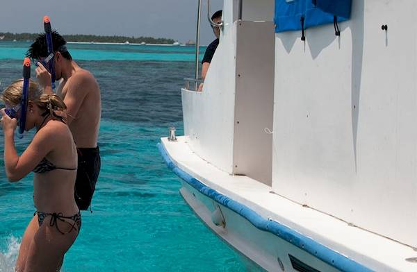 Ein Paar, das im Meer schnorchelt, steht neben einem Boot am Meeru Island Resort & Spa.