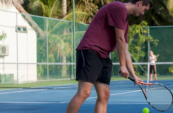 Tennisspieler in einem roten T-Shirt schlägt einen Ball auf einem blauen Tennisplatz.