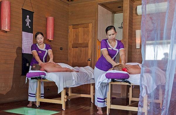 Massagebehandlung im Meeru Island Resort & Spa mit zwei Therapeutinnen und zwei Patienten auf Liegen.
