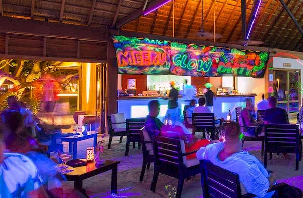 Loungebereich des Meeru Island Resort & Spa mit bunten Lichtern und Menschen, die sitzen und unterhalten.