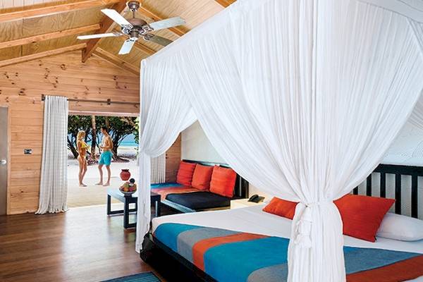 Schlafzimmer im Meeru Island Resort & Spa mit Bett, Vorhängen, Deckenventilator und Fernseher.