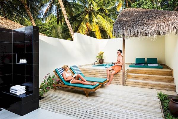 Zwei Personen entspannen sich auf Liegen im Außenbereich des Meeru Island Resort & Spa.
