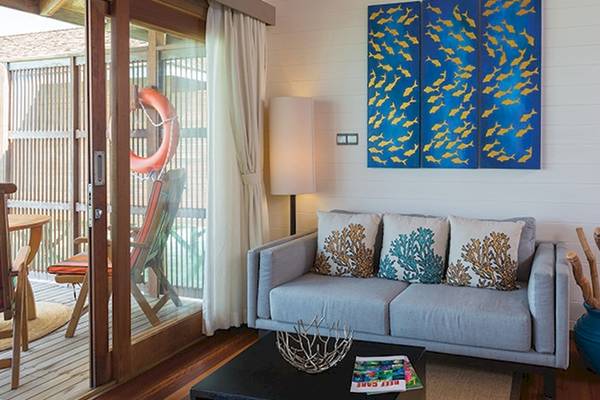 Wohnbereich im Meeru Island Resort mit grauem Sofa, dekorativen Kissen und blauer Wanddekoration.