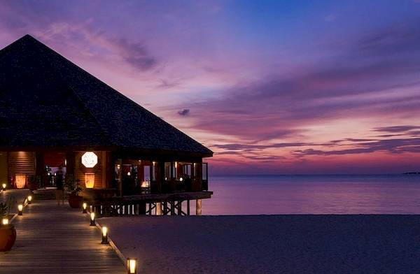 Das Meeru Island Resort & Spa bei Sonnenuntergang mit einem Weg und Laternen.