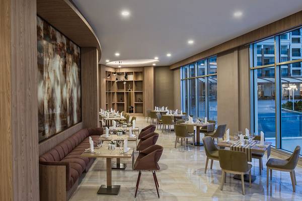 Innenansicht des Grape Kiss Restaurants im Delphin BE Grand Resort mit Tisch und Stühlen, Wandmalerei und großen Fenstern.