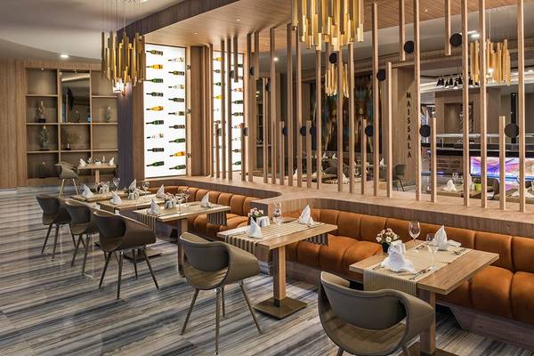 Innenansicht des Restaurants im Delphin BE Grand Resort mit braunen Sofas, Holztischen und goldenen Kronleuchtern.
