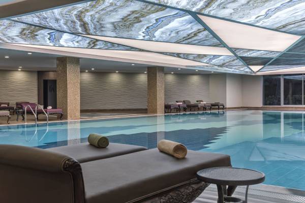 Innenpool des Delphin BE Grand Resort mit Marmordecke und Liegen.