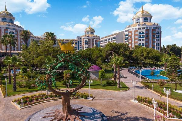 Luxuriöses Delphin BE Grand Resort mit Palmen, Gärten und einer Statue in der Vorderansicht unter klarem Himmel.