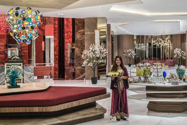 Elegante Hotellobby des Delphin BE Grand Resort mit einer lächelnden Kellnerin und einer farbenfrohen Deckenleuchte.