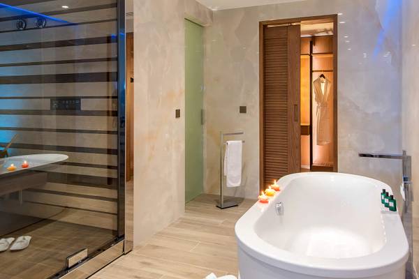 Badezimmer im Nana Princess Suites mit Sauna und Badewanne, gefüllt mit Wasser und brennenden Kerzen.