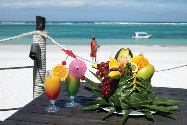 Cocktails und Obstkorb auf einem Tisch am Strand des Diani Reef Beach Resort & Spa