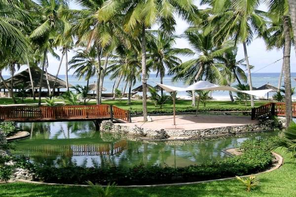 Gartenansicht des Diani Reef Beach Resort & Spa mit Brücke, Teich und Palmen