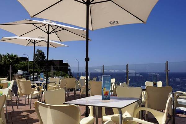 Hotelterrasse mit Meerblick, Bahia Flamingo, gedeckte Tische und Stühle unter Schirmen.