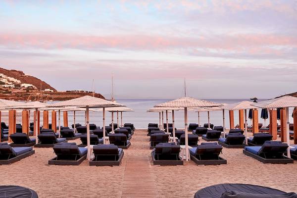 Strandbereich des Mykonos Ammos Hotels mit vielen Liegen und Sonnenschirmen bei Sonnenuntergang