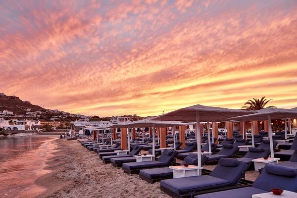 Strand des Mykonos Ammos Hotels mit vielen Liegen und Sonnenschirmen bei Sonnenuntergang