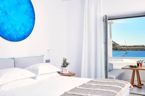 Innenansicht eines Zimmers im Mykonos Ammos Hotel mit Bett, Kissen und Meerblick.