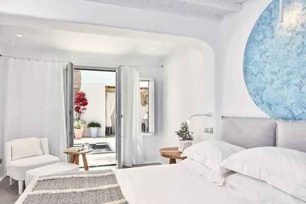 Schlafzimmer im Mykonos Ammos Hotel mit weißem Bett, Kissen, Tisch, Pflanze und offenem Fenster