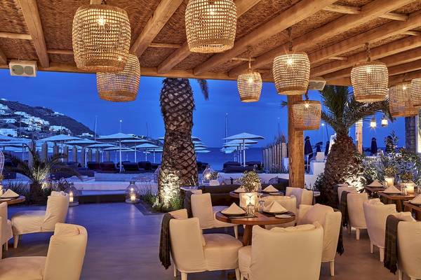 Terrasse des Mykonos Ammos Hotels bei Nacht mit beleuchteten Lampen und Tischen im Freien.