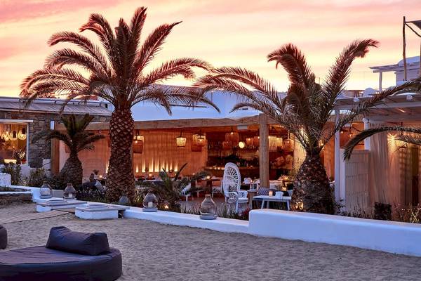 Sonnenuntergangsansicht des Mykonos Ammos Hotels mit Palmen und Außenbeleuchtung.