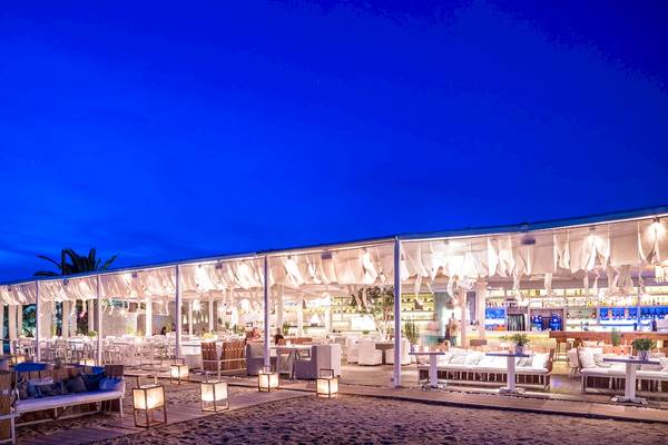 Nachtansicht des Mykonos Ammos Hotel-Strand-Lounge-Bereichs mit weißen Möbeln und Beleuchtung.