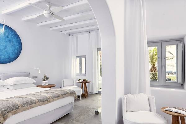Schlafzimmer im Mykonos Ammos Hotel mit weißen Wänden, Bett, Nachttischen und Deckenventilator.