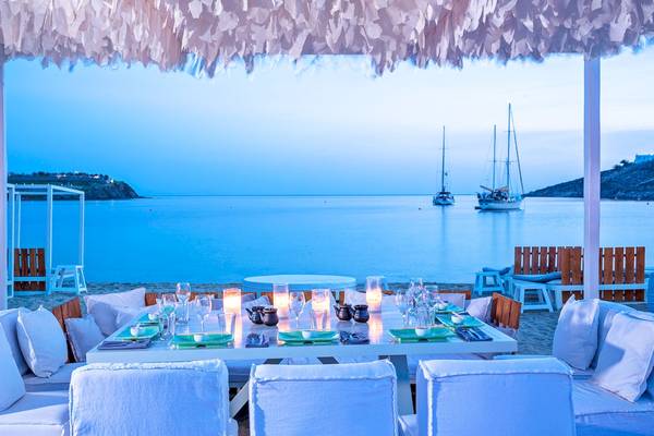 Restauranttisch im Mykonos Ammos mit Blick aufs Meer und zwei Segelboote im Hintergrund.