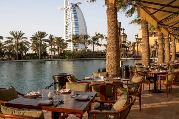Außenbereich des Jumeirah Mina A'Salam Hotels mit einem Restaurant am Wasser, Blick auf die Palmen und das Burj Al Arab Hotel.