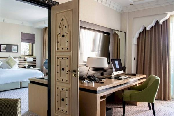 Ein Hotelzimmer mit Schreibtisch, grünem Stuhl und Laptop, Bett und Fenstern.
