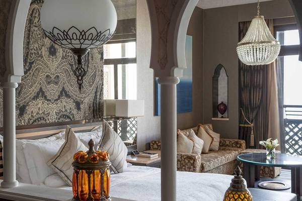 Innenansicht des Schlafzimmers im Jumeirah Mina A'Salam Hotel mit großen Bögen, Kronleuchtern, einem Bett, einem Tisch und einem Sofa.