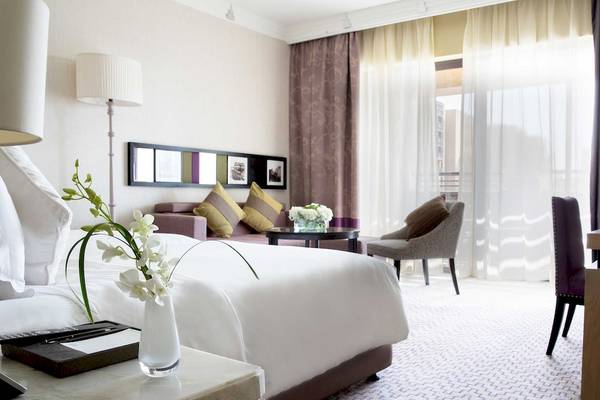 Innenansicht eines Hotelzimmers im Jumeirah Mina A'Salam mit Bett, Tisch, Stuhl und Fenstern.