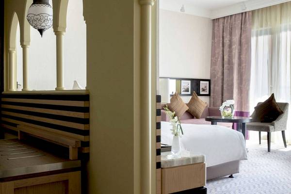 Innenansicht des Jumeirah Mina A'Salam Hotelzimmers mit Bett, Sitzbereich und Fenstern.