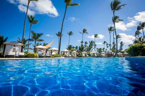 Ein großer Swimmingpool im Majestic Elegance Punta Cana Hotel mit Sonnenschirmen und Palmen im Hintergrund.