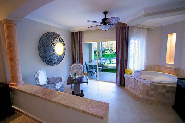 Innenansicht der Suite im Majestic Elegance Punta Cana mit Wohnzimmer, Esstisch und Whirlpool.